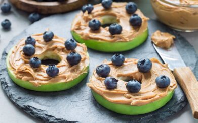 Green apple rounds with peanut butter and blueberries on slate board
