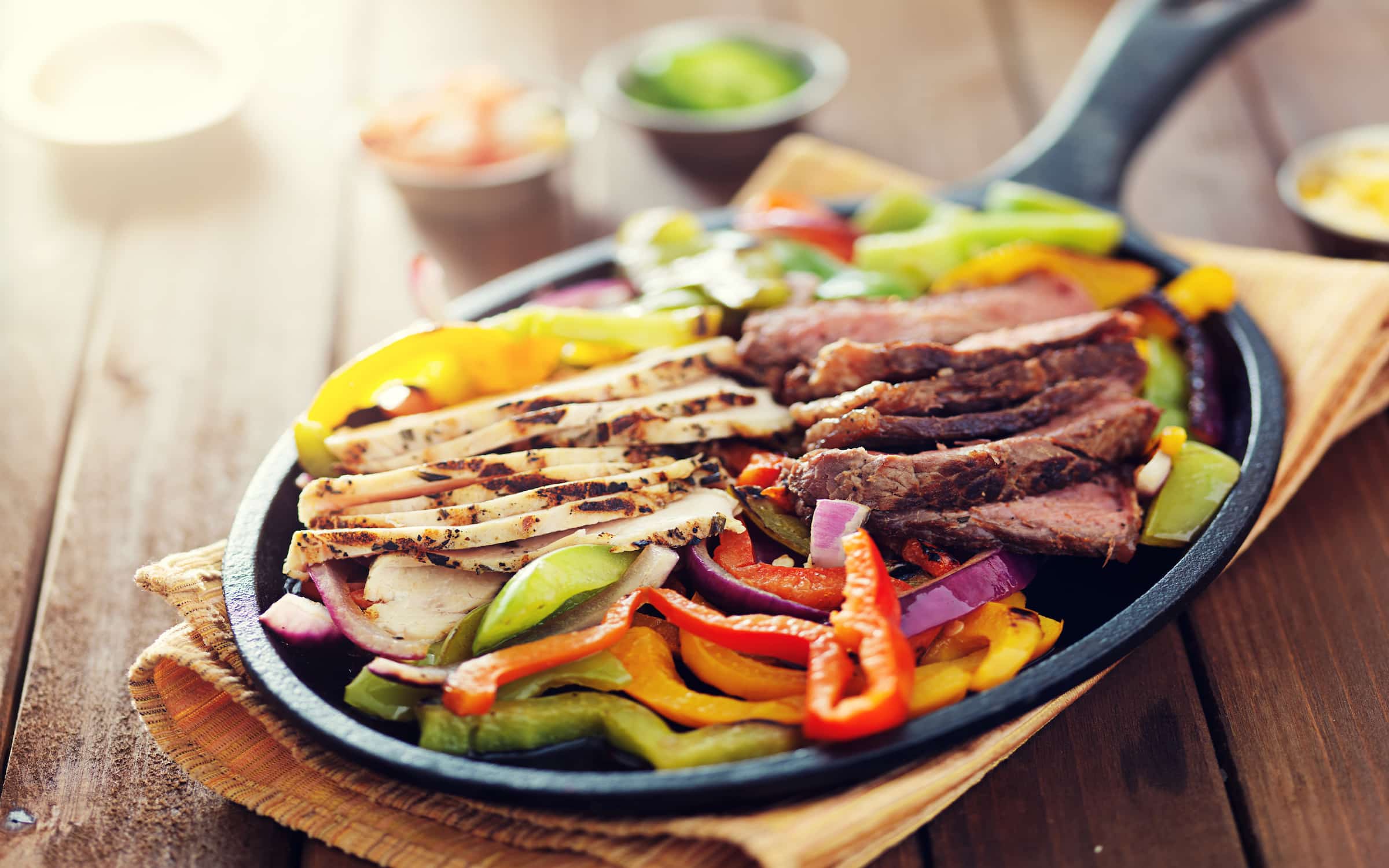skillet fajitas with steak and chicken on rustic wooden table
