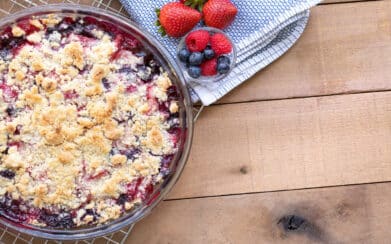 Flat lay of a berry cobbler and spring berries, on a wood table with space for text on the right